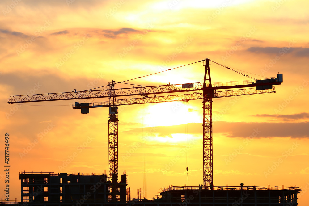 construction with tower cranes on a bright sunset background