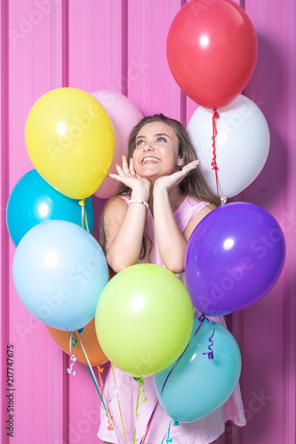 Birthday girl with colored balloons against metal rose wall.