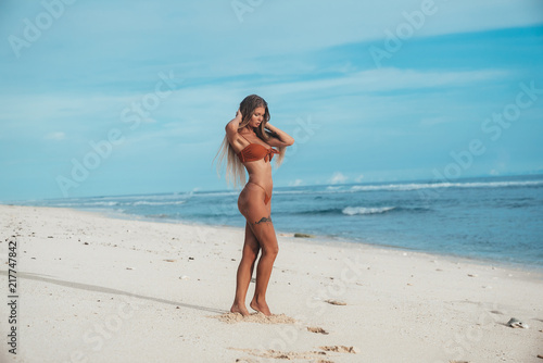 A young beautiful model with long legs in a swimsuit on the beach wants to go swimming  iron his long white hair  has a small tattoo on his hip.