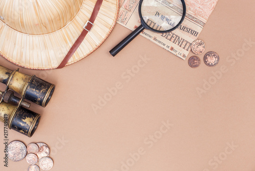 top view on items for travel  recreation and adventure  map  vintage paper and coins  magnifying glass and safari hat on a beige background with space for text as a frame. flat lay