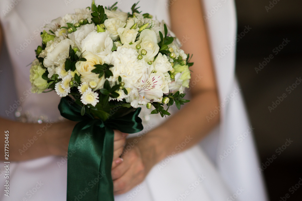 The bride in white dress holds beautiful bouquet of white flowers and greenery in her hands. The bride in white dress holds beautiful bouquet of white flowers and greenery in her hands.