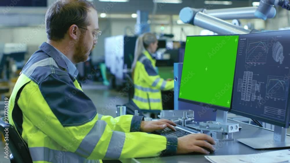 At the Factory: Mechanical Engineer Works on the Green Mock-up Screen Personal Computer with Two Displays, Second Display Shows Graphics Blueprint for Engine for Robotic Arm. At the Factory: Mechanical Engineer Works on the Green Mock-up Screen Personal Computer with Two Displays, Second Display Shows Graphics Blueprint for Engine for Robotic Arm.