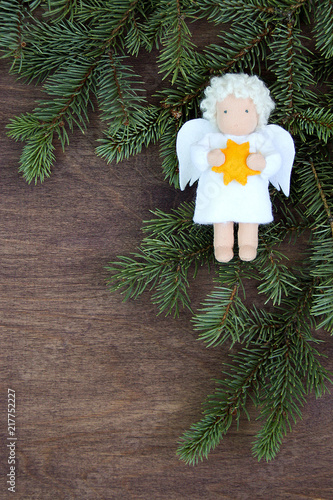 White felt Christmas angel with yellow star in hands to fresh natural branches of Christmas tree spruce on wooden background
