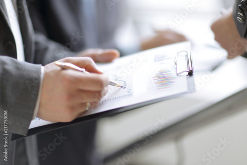 businessman at desk checking a financial report and pointing at a bar chart with a pen