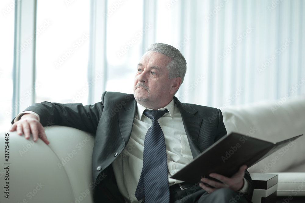 pensive businessman with clipboard sitting on the office couch pensive businessman with clipboard sitting on the office couch