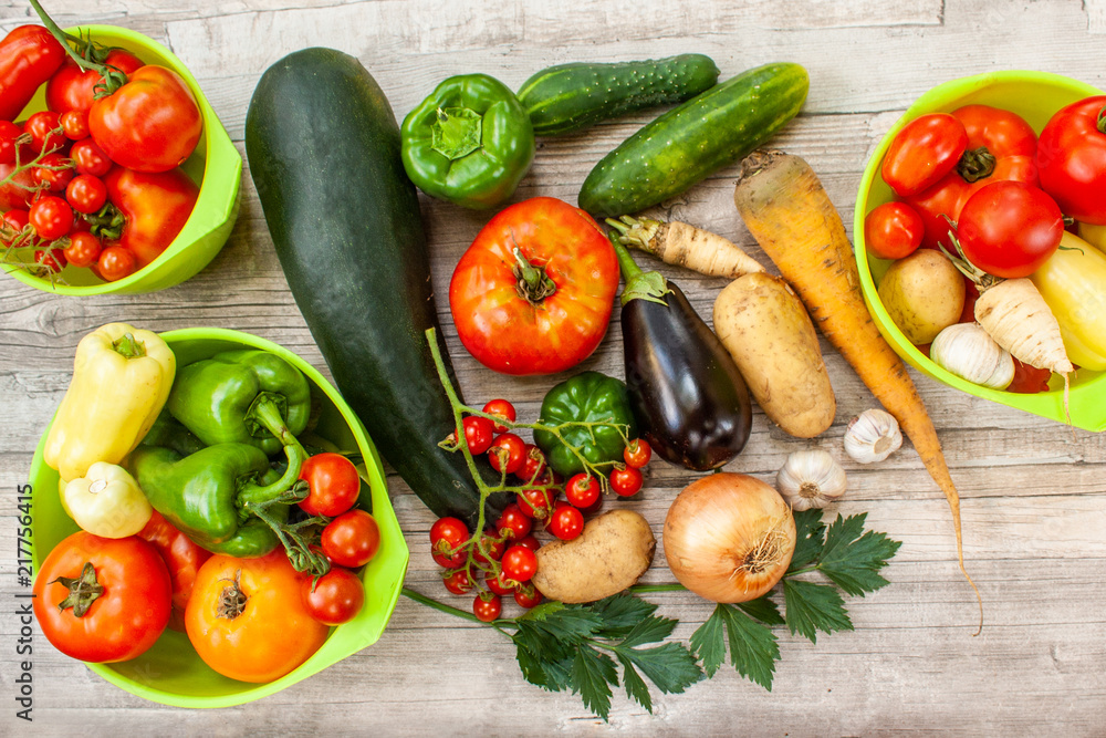 Colourful variety of fresh home grown vegetables from an organic garden on a wooden surface. Tomato, green and yellow bell peppers, carrot, parsley, onion, garlic, potato, eggplant and zucchini. Colourful variety of fresh home grown vegetables from an organic garden on a wooden surface. Tomato, green and yellow bell peppers, carrot, parsley, onion, garlic, potato, eggplant and zucchini.