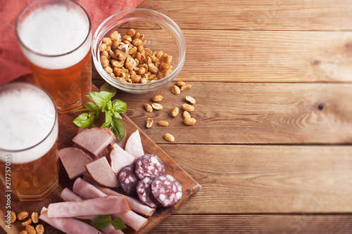 Variety of meat snacks to beer: ham, rolled meat, with fresh basil and glass beer over dark wooden background. Top view, copy space.
