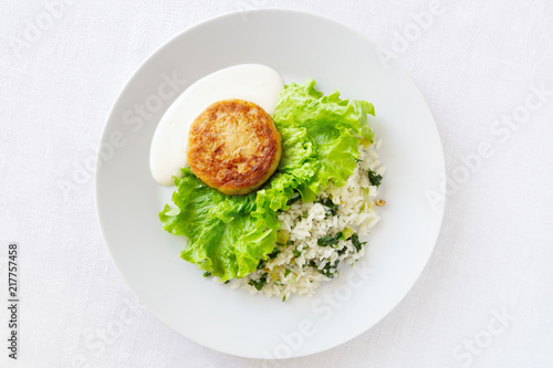 cabbage cutlet on lettuce leafs garnished with rice with leek, spinach, green onion, parsley, and dill served with mayo and sour cream sauce
