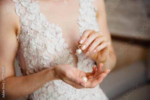 Close-up of a cropped frame of a girl in a white lace dress with embroidery holding in hands a pearl earring. The bride is going to the wedding.