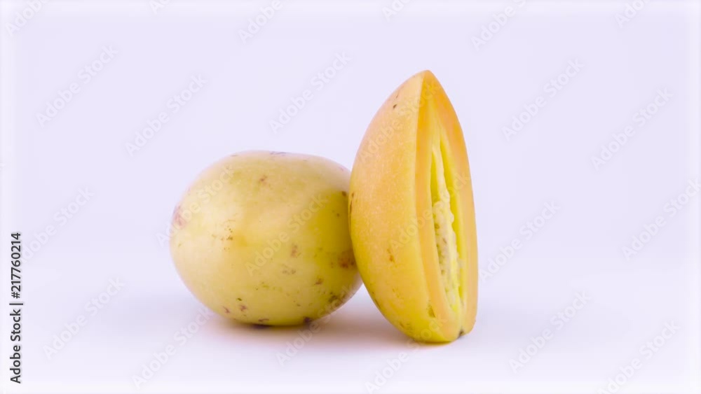 One whole and one half cut mature yellow pepino fruits rotating on the turntable. Isolated on the white background. Closeup. Macro. One whole and one half cut mature yellow pepino fruits rotating on the turntable. Isolated on the white background. Closeup. Macro.