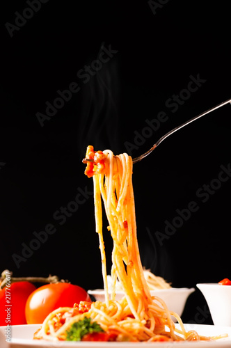 Photography Hot spaghetti with tomato sauce in white plate,  food stylish action with black background, pull spaghetti up with fork