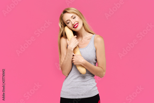 Young beautiful girl with a pink background eating a baguette and smiling. Concept of un healthy fat junk and healthy food