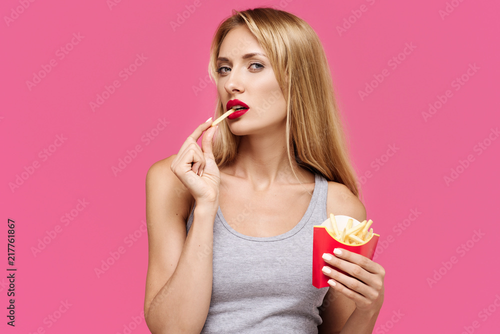 Young beautiful slender girl with a pink background eating a french fries. Concept of un healthy fat junk and healthy food Young beautiful slender girl with a pink background eating a french fries. Concept of un healthy fat junk and healthy food