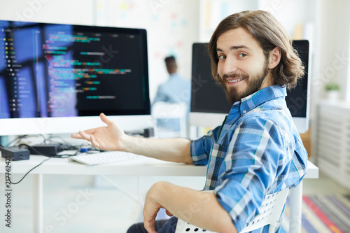 Young successful specialist in data decoding sitting by workplace and pointing at computer monitor photo