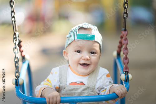 Baby boy in a cap and beige corduroy jumpsuit having fun on a swing.