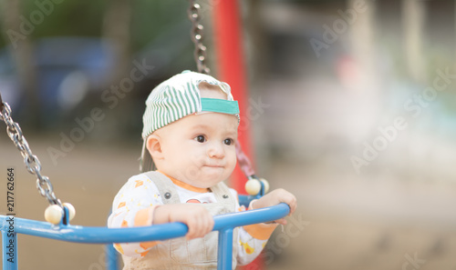 Baby boy in a cap and beige corduroy jumpsuit having fun on a swing. Copyspace