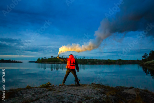 A man stands on an island with a torch in his hand. Smoke bomb. A signal for help. The man in the rescue jelly. At night, a man signals a smoke sword.