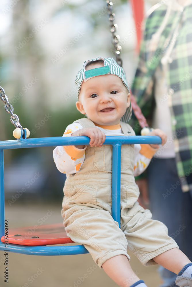 Baby boy in a cap and beige corduroy jumpsuit having fun on a swing. Copyspace Baby boy in a cap and beige corduroy jumpsuit having fun on a swing. Copyspace