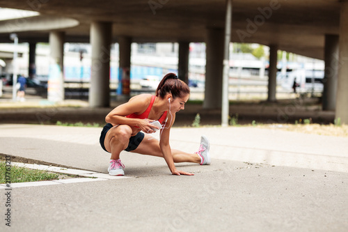 Female runner stretching and relaxing on city street after jogging.