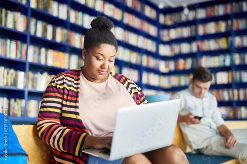 Bild auf Leinwand Concentrated portly African-American student girl with hair bun using laptop whi