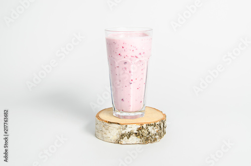 Glass of yoghurt cocktail, smoothies, with berries stands on a birch stump on white background.