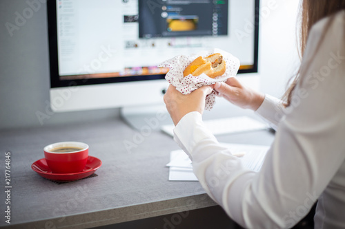Young business woman eating burger with coffee at the workplace in office