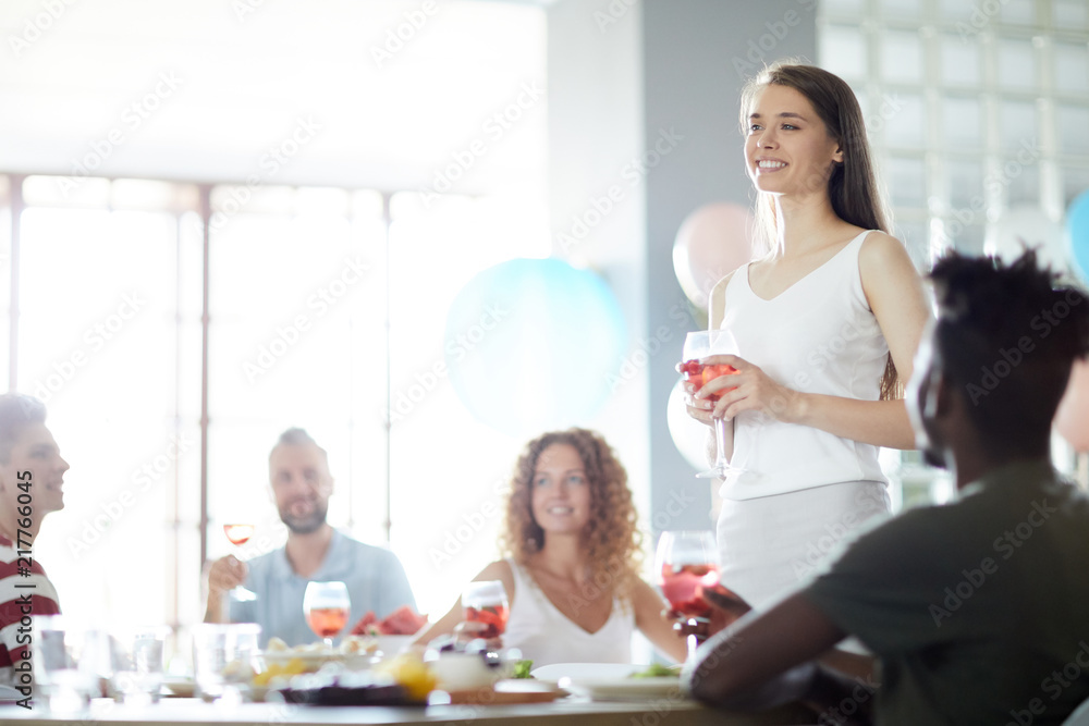 One of happy guests pronouncing toast while standing by festive table among friends One of happy guests pronouncing toast while standing by festive table among friends