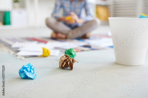 Crumpled colorful papers lying on the floor next to trash bin with businesswoman on background