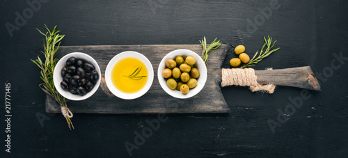 Fototapeta Naklejka Na Ścianę i Meble -  A set of olives and olive oil and rosemary. Green olives and black olives. On a black wooden background. Free space for text.