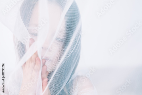 child purity and innocence. romantic and beautiful poetical and elated portrait of a wistful and pensive dreamy girl behind the net curtain.