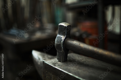 Close-up of steel hammer placed on anvil in dark workshop, blacksmiths tools concept