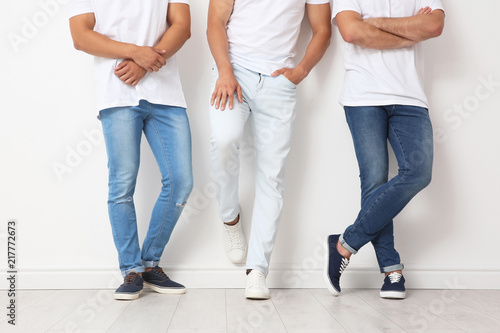 Group of young men in jeans near light wall