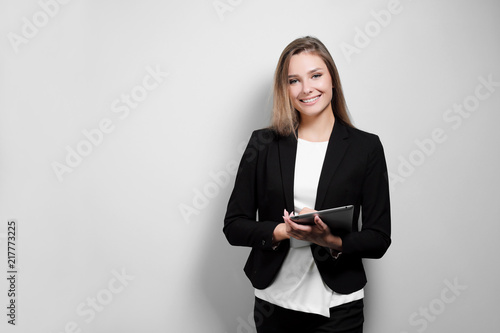 Portrait of a beautiful smiling woman blonde with a tablet in her hands in a business suit and jacket on a white background. A student or a businesswoman is working. photo