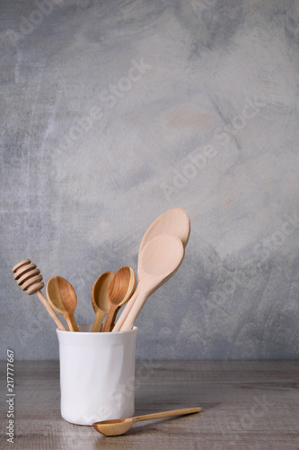  A set of wooden spoons in a white bowl on a gray background on a wooden table