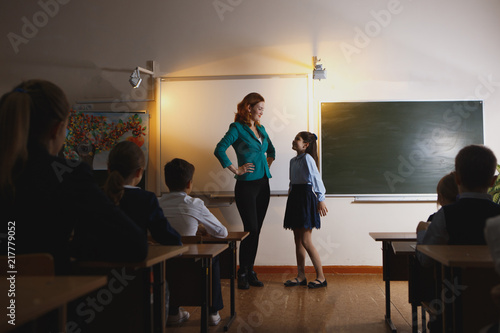 Smiling elderly teacher near the chalkboard asking student at the math lesson