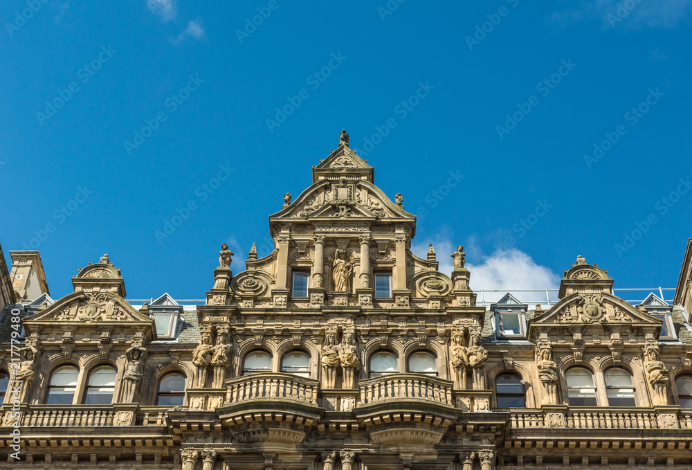 Edinburgh, Scotland, UK - June 13, 2012: Top of monumental brown stone facade of Department store on corner of Princess and South David streets under blue sky.