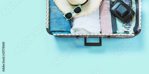 Open suitcase with female clothes for trip on pastel blue. Top view with copy space. Summer concept travel.