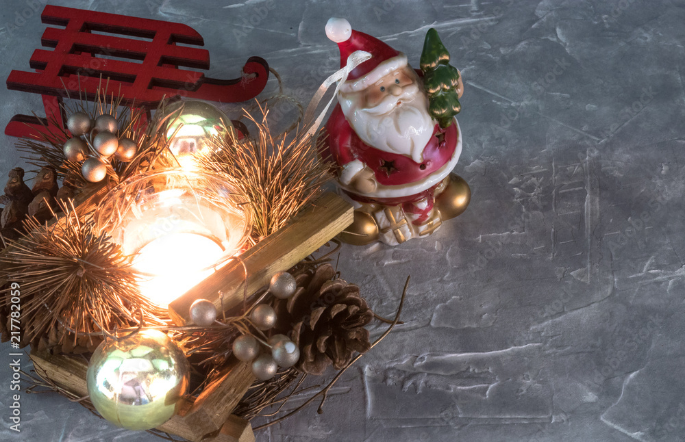 a Santa Claus toy, a burning candle and a sleigh. Christmas Holidays. set of Christmas ornaments on gray concrete with copy space for your text.new concept. a Santa Claus toy, a burning candle and a sleigh. Christmas Holidays. set of Christmas ornaments on gray concrete with copy space for your text.new concept.