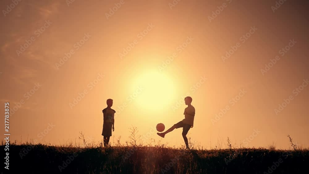 Two boys playing soccer at sunset. Silhouette of children playing with a ball at sunset. The concept of a happy family Two boys playing soccer at sunset. Silhouette of children playing with a ball at sunset. The concept of a happy family