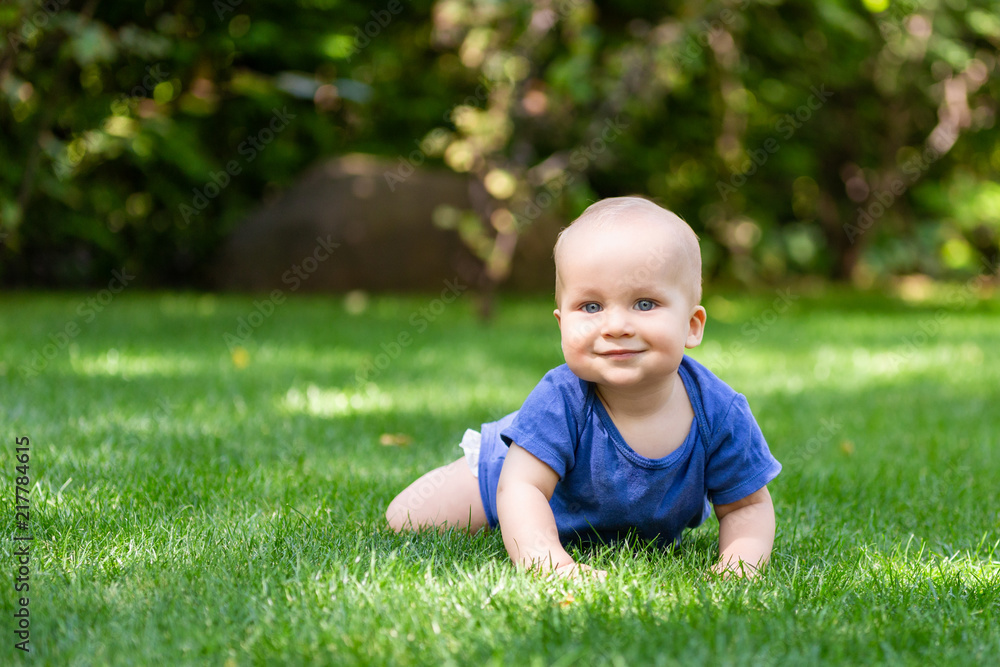 Cute little blond baby boy crawling on fresh green grass. Kid having fun making first steps on mowed natural lawn. Happy and healthy childhood concept Cute little blond baby boy crawling on fresh green grass. Kid having fun making first steps on mowed natural lawn. Happy and healthy childhood concept