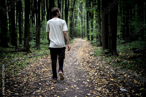lonely young male hipster in casual walks in the autumn dark moody forest with fallen leaves