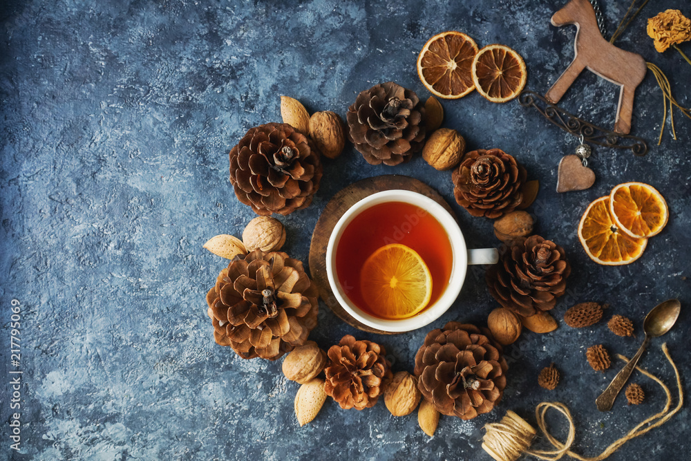 Cozy autumn morning with cup of tea with lemon, decorative corns, dried oranges, nuts and wooden toys on dark blue background, teatime, hugge concept, selective focus, top view