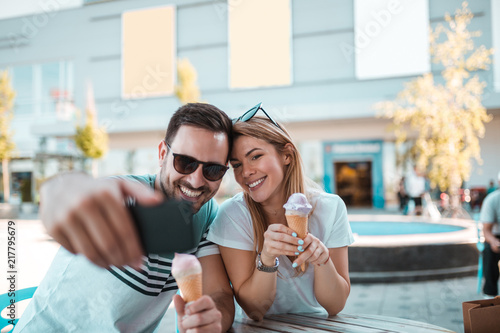 Young man with sunglasses is taking selfie with his girlfriend while they having ice-cream outdoors