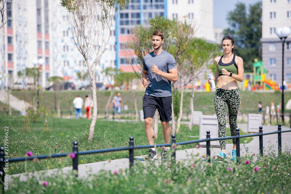 Obraz premium Full length portrait of modern young couple running together outdoors in city park on sunny Summer day, copy space