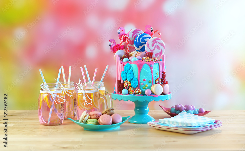 On-trend candyland fantasy drip cake for children's, teen's birthday, anniverary, mother's day and valentine's day celebrations. in party table setting with mason jars pink lemonade.