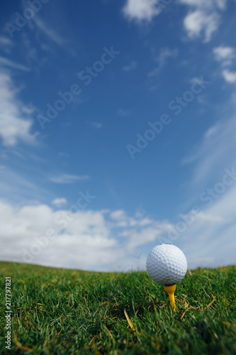 golf ball on tee, green grass and blue sky background