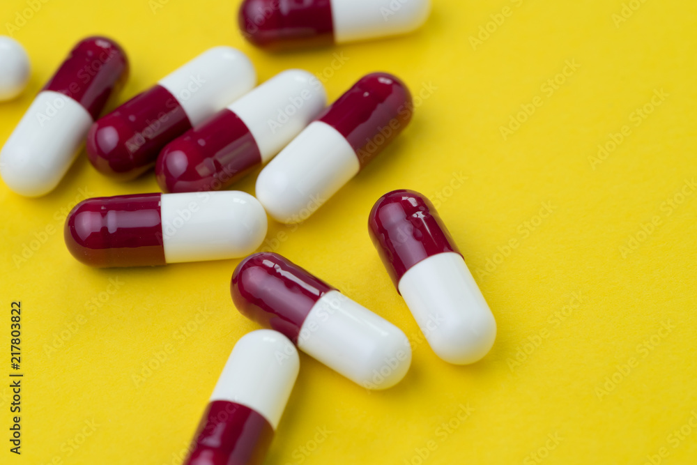 Dark red and white capsules pills on yellow background with copy space, phamacy or healthcare, drug and science concept