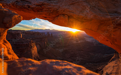 Cliff s-edge sandstone Mesa Arch framing an iconic sunrise view of the red rock canyon landscape below.