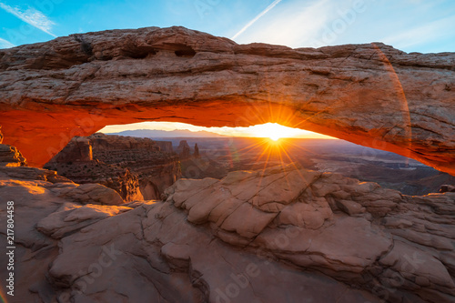 Cliff s-edge sandstone Mesa Arch framing an iconic sunrise view of the red rock canyon landscape below.