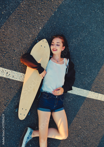 Skater girl lying down on asphalt surface of the road and enjoing summer warm weather after phisical activity photo